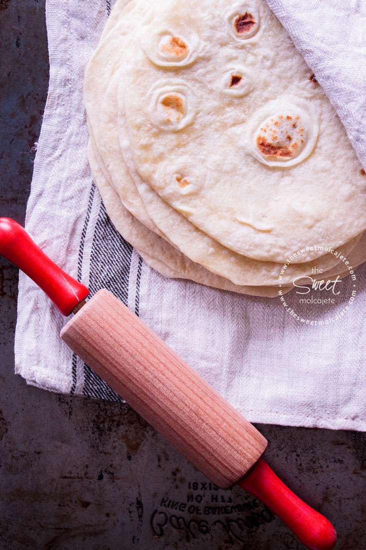 Vista de arriba a varias tortillas de harina apiladas con un rodillo a lado