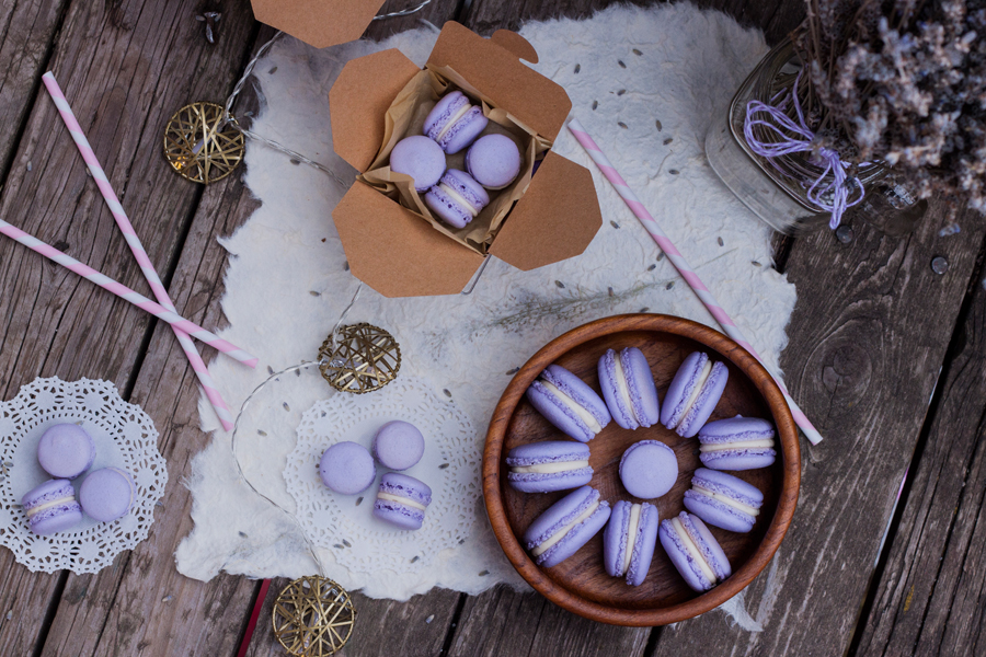 Mesa con varios macarons en plato de madera y cajitas de carton, hay luces y un florero