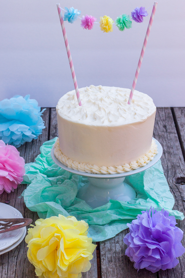 Pastel de cumpleaños con betún de queso crema con una guirnalda de flores de papel  adornando arriba