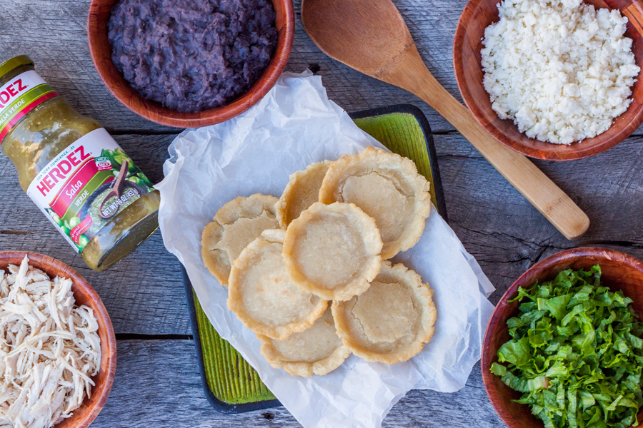 vista de arriba a un plato con sopes recién hechos y los platos con ingredientes para prepararlos
