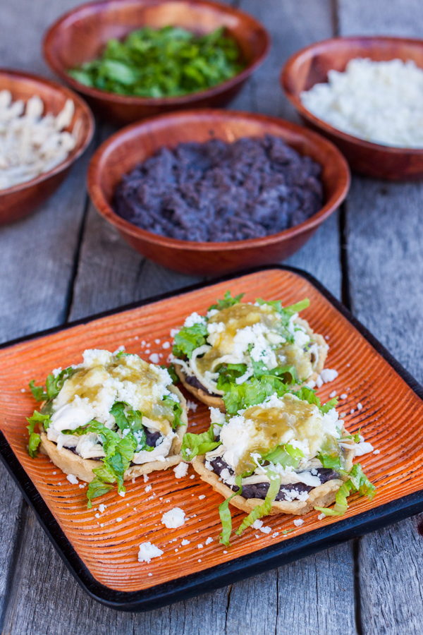 # sopes de pollo en un plato de madera, los sopes llevan frijoles, pollo, crema, queso, lechuga y salsa verde