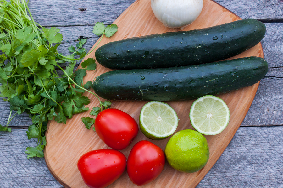 tabla de picar con pepinos, jitomates, limones partidos, cebolla y cilantro