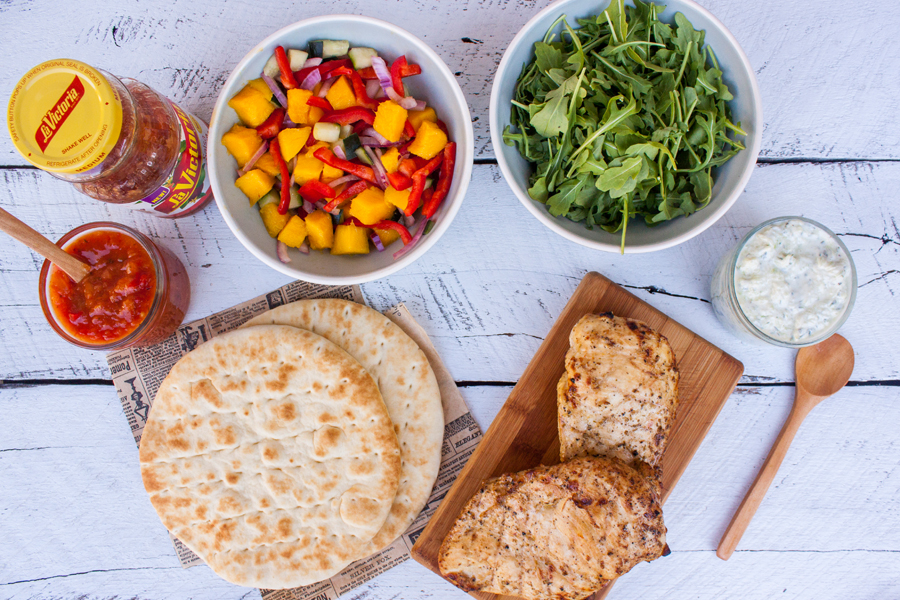 mesa con ingredientes para preparar unos gyros de pollo (salsa La Victoria, ensalada de mango, pollo, pan pita, salsa Tzatziki y arúgula)