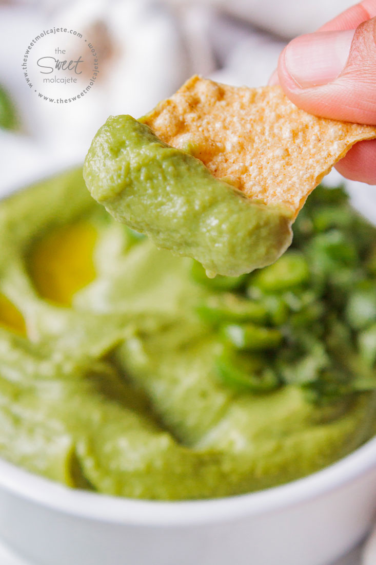 Mano agarrando un totopo con Hummus Verde de Cilantro con Chile